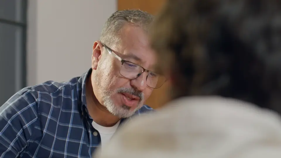 Homem de óculos conversa com atenção com uma colega, frente a frente