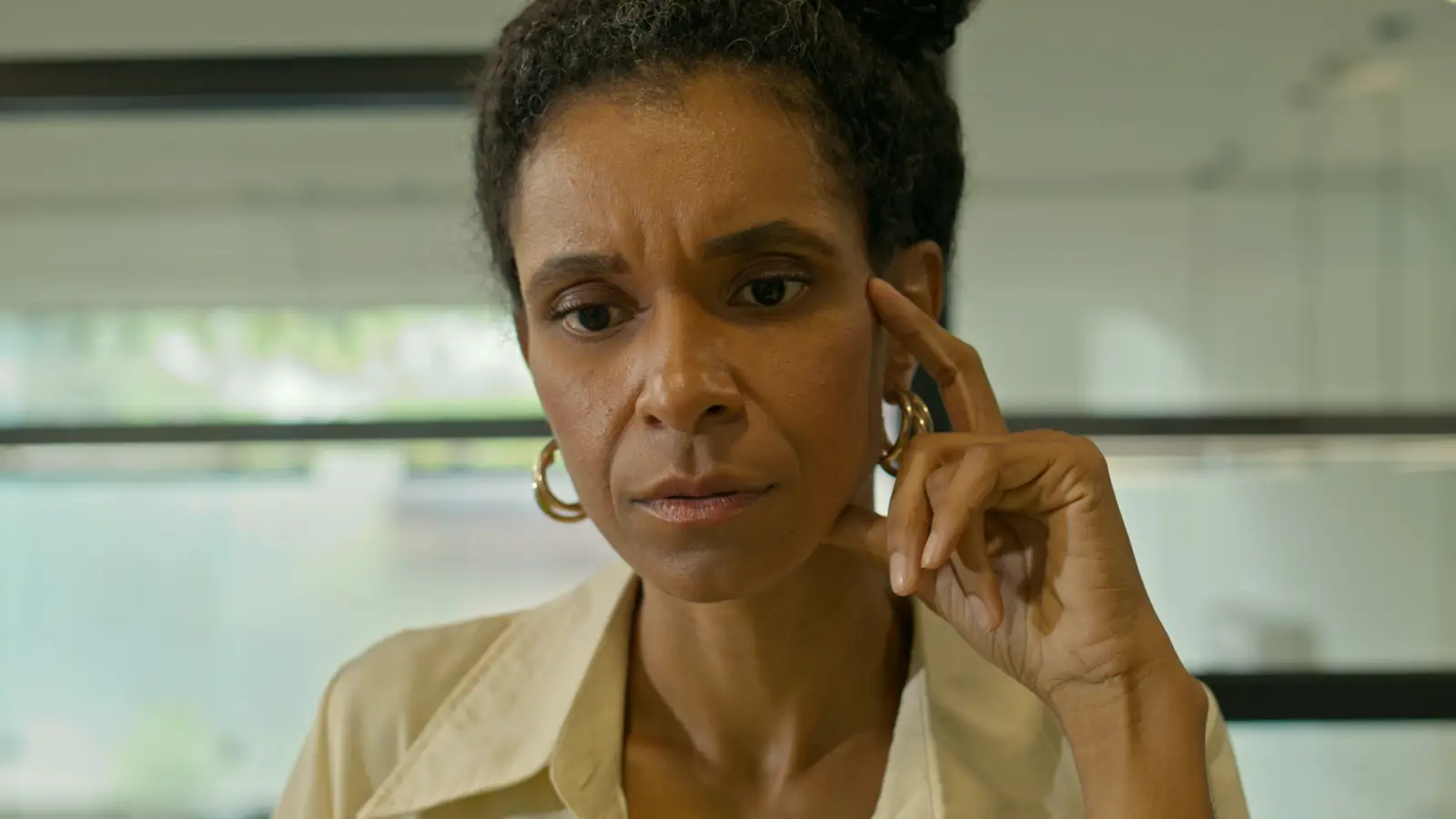 Mulher negra, de meia-idade, pensativa no escritório, com a mão na têmpora